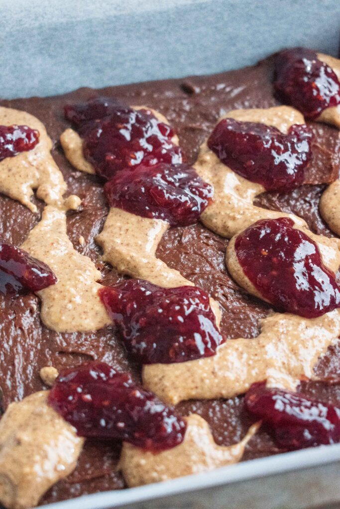 dollops of peanut butter and jam on top of the Peanut Butter and Jam Brownies mixture