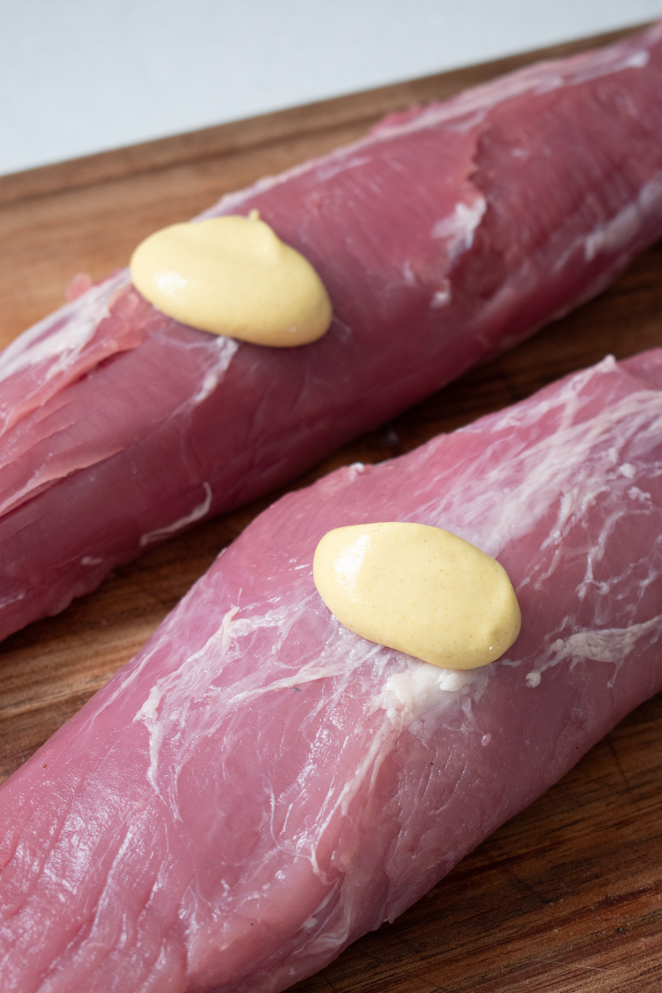 #porktenderloin raw pork tenderloin on a wooden board with a dash of mustard on top